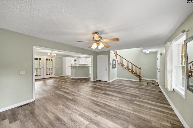 unfurnished living room with visible vents, wood finished floors, stairs, and ceiling fan with notable chandelier