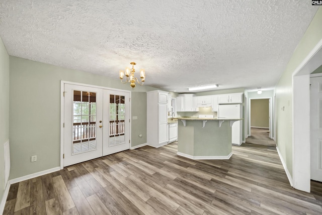 kitchen with wood finished floors, an inviting chandelier, freestanding refrigerator, white cabinets, and a kitchen breakfast bar