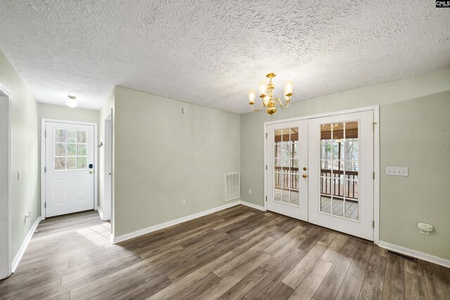 unfurnished dining area with wood finished floors, a notable chandelier, french doors, and visible vents