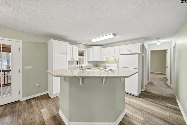 kitchen with a kitchen bar, white appliances, white cabinets, and a sink