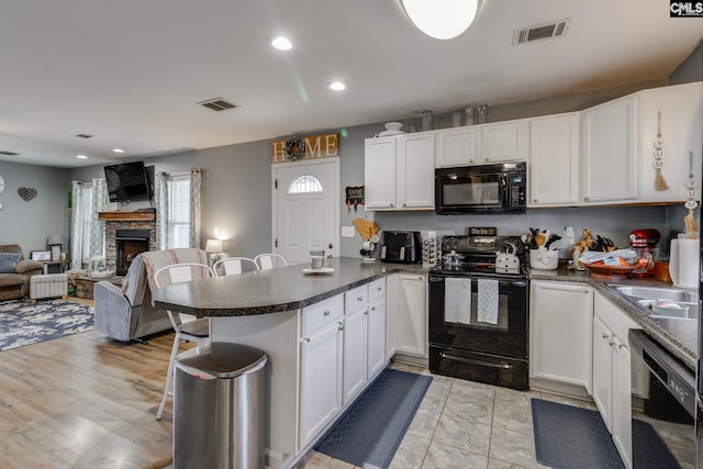 kitchen with visible vents, white cabinetry, a peninsula, and black appliances