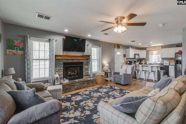 living area with visible vents, a stone fireplace, ceiling fan, and wood finished floors