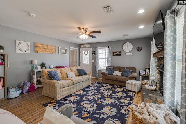 living area with ceiling fan, visible vents, wood finished floors, and a fireplace