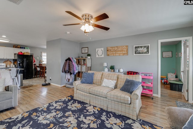 living area featuring light wood finished floors, baseboards, and a ceiling fan