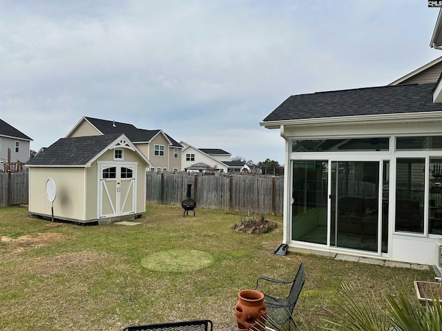 view of yard featuring an outbuilding, a fenced backyard, a shed, and a sunroom