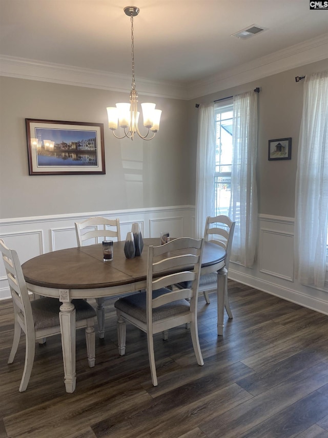 dining space featuring visible vents, a wainscoted wall, dark wood-type flooring, ornamental molding, and a chandelier