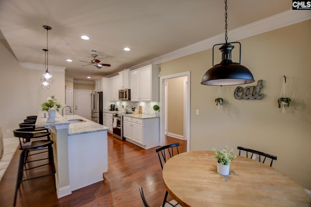 kitchen featuring a breakfast bar, decorative backsplash, appliances with stainless steel finishes, white cabinets, and a sink