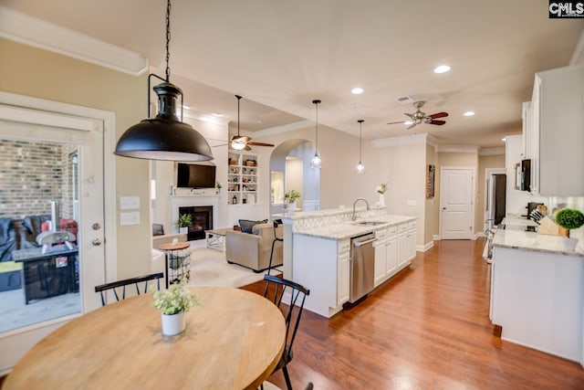 dining space featuring a glass covered fireplace, wood finished floors, a ceiling fan, and arched walkways