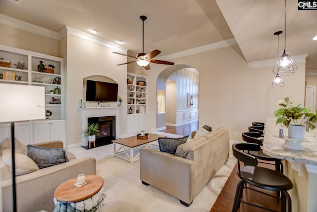 living area with arched walkways, built in shelves, a ceiling fan, and ornamental molding