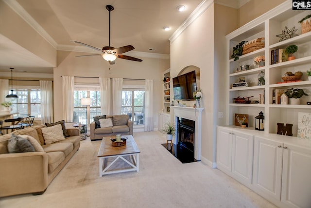 living area featuring a fireplace with flush hearth, built in features, ornamental molding, light carpet, and a ceiling fan