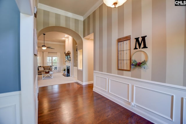 hallway with wallpapered walls, crown molding, arched walkways, and wainscoting