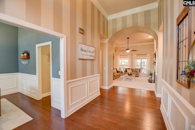 entrance foyer featuring wallpapered walls, a wainscoted wall, arched walkways, and dark wood-type flooring