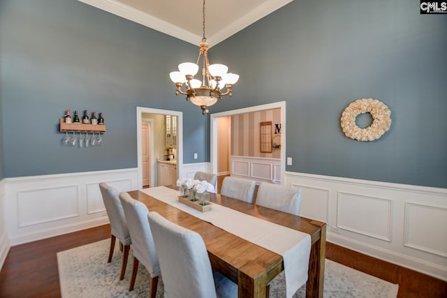 dining room with a wainscoted wall, dark wood-style floors, a chandelier, and ornamental molding