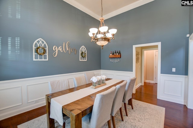 dining room featuring wood finished floors, ornamental molding, vaulted ceiling, wainscoting, and a chandelier