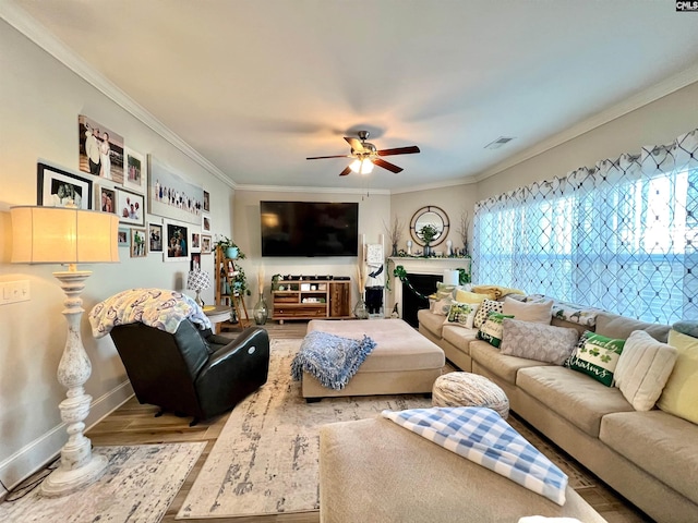 living area featuring visible vents, crown molding, baseboards, wood finished floors, and a ceiling fan