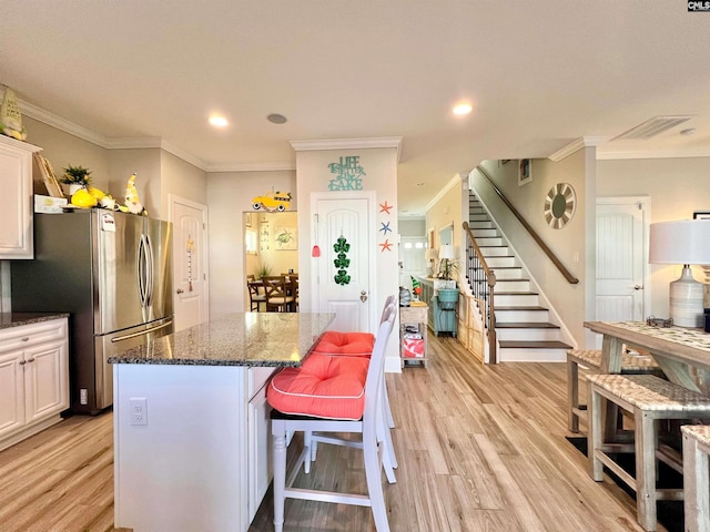 kitchen with a kitchen island, dark stone countertops, freestanding refrigerator, light wood-style floors, and white cabinets