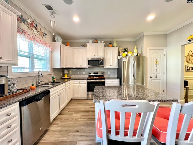 kitchen with light wood finished floors, ornamental molding, appliances with stainless steel finishes, and a sink