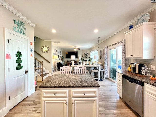 kitchen with stainless steel dishwasher, dark stone counters, light wood finished floors, and ornamental molding