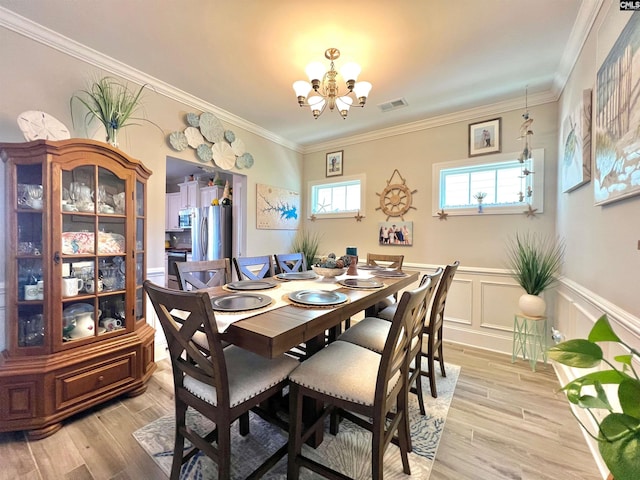 dining area featuring a wainscoted wall, visible vents, crown molding, a notable chandelier, and light wood-type flooring