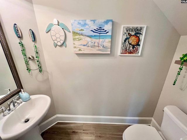 half bath featuring a sink, baseboards, toilet, and wood finished floors