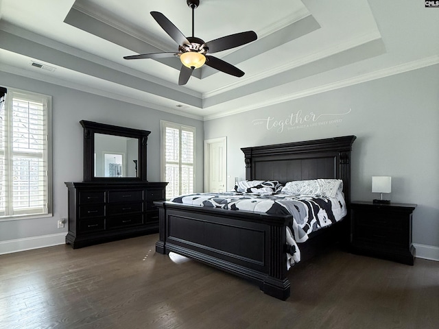 bedroom with visible vents, baseboards, a tray ceiling, ornamental molding, and wood finished floors