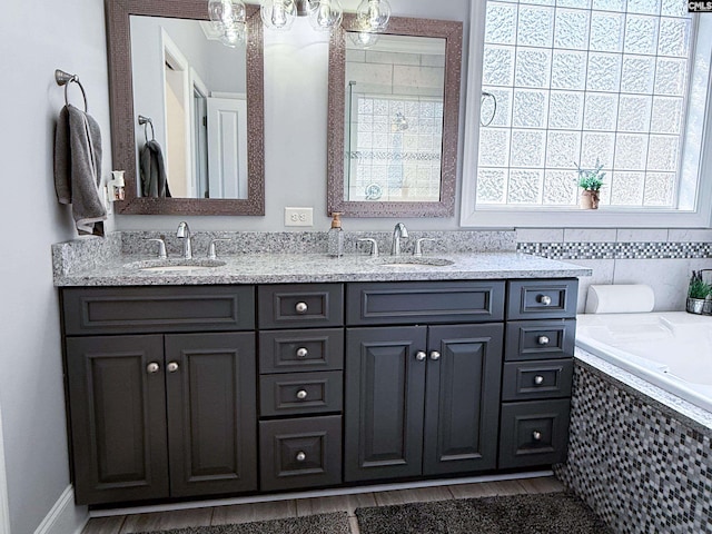 full bathroom featuring double vanity, wood finished floors, tiled tub, and a sink