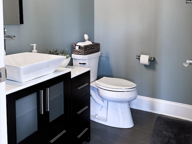 half bathroom featuring vanity, toilet, wood finished floors, and baseboards