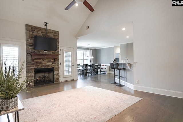 living area with visible vents, a ceiling fan, wood finished floors, a stone fireplace, and baseboards