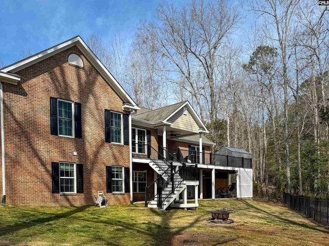 rear view of property featuring a ceiling fan, an outdoor fire pit, stairs, a lawn, and brick siding