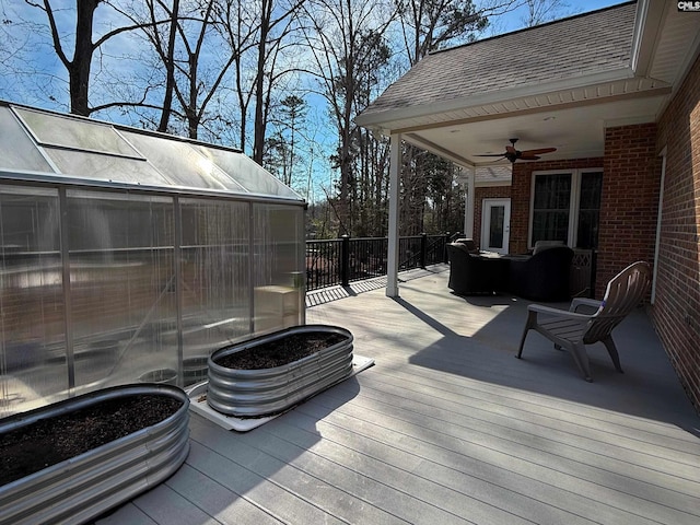 wooden terrace featuring a greenhouse, an outbuilding, and a ceiling fan