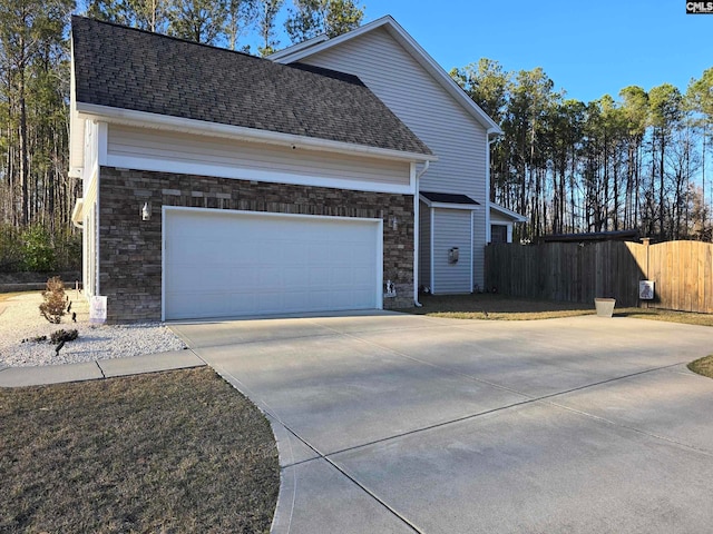 view of side of property featuring fence, an attached garage, a shingled roof, concrete driveway, and stone siding