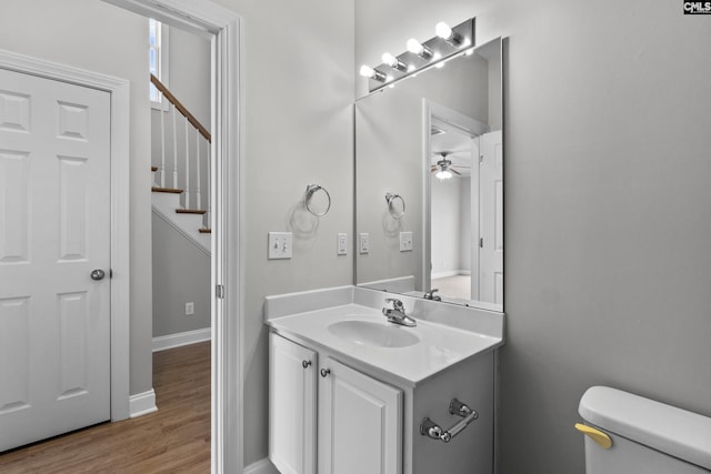 half bathroom with vanity, wood finished floors, baseboards, ceiling fan, and toilet