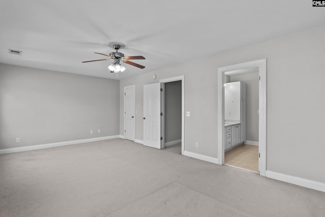 unfurnished bedroom with visible vents, connected bathroom, baseboards, light colored carpet, and ceiling fan