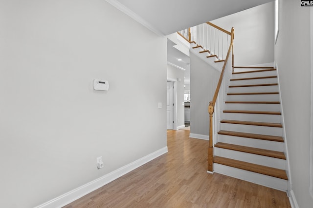 stairs featuring crown molding, a high ceiling, wood finished floors, and baseboards