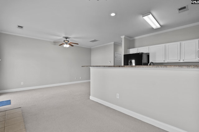 kitchen featuring visible vents, ceiling fan, light carpet, black fridge, and white cabinetry