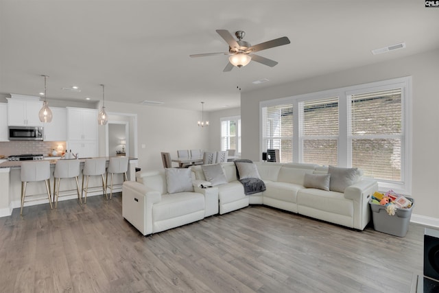 living area with visible vents, ceiling fan with notable chandelier, baseboards, and wood finished floors