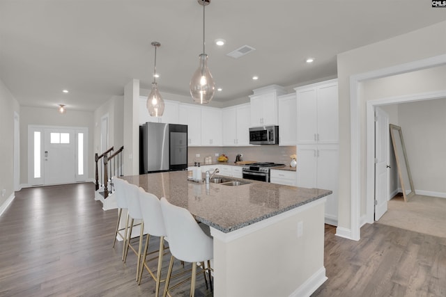 kitchen featuring visible vents, a sink, dark stone counters, stainless steel appliances, and a kitchen island with sink