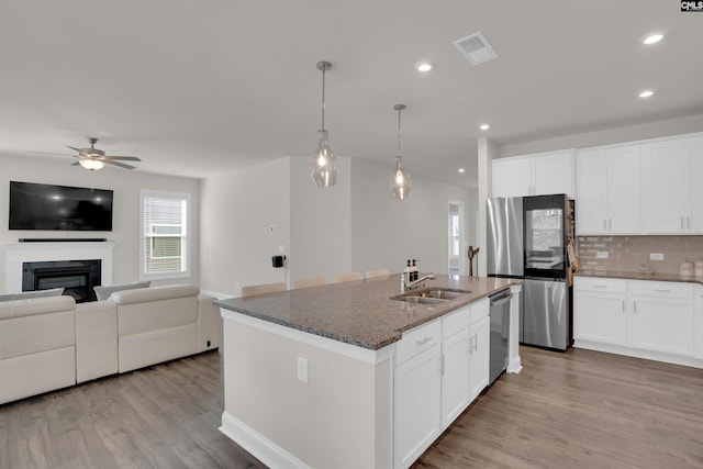 kitchen with a sink, dark stone countertops, backsplash, open floor plan, and stainless steel appliances