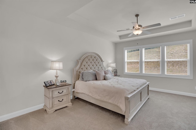 bedroom with visible vents, light colored carpet, a raised ceiling, and baseboards