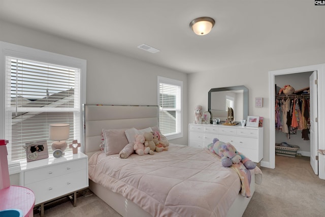 bedroom featuring a walk in closet, light colored carpet, visible vents, and a closet