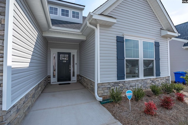 view of exterior entry with stone siding and roof with shingles