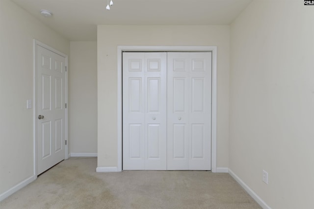 unfurnished bedroom featuring a closet, baseboards, and light colored carpet