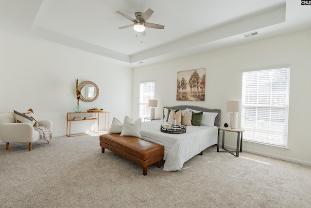 carpeted bedroom with visible vents, baseboards, a tray ceiling, and a ceiling fan