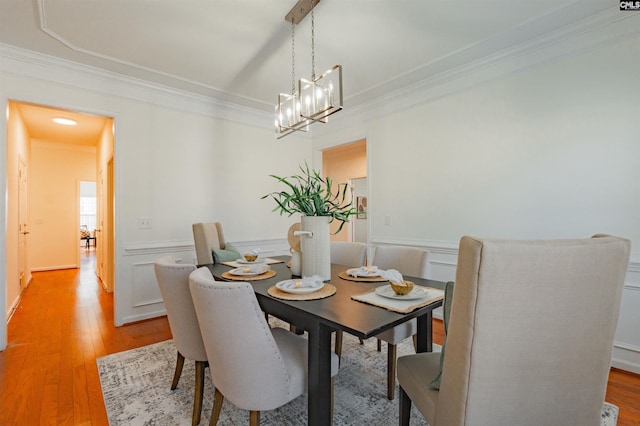 dining area featuring a wainscoted wall, crown molding, a decorative wall, and light wood-type flooring