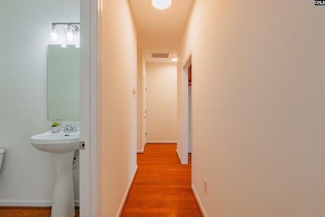 corridor with light wood-style flooring, baseboards, visible vents, and a sink