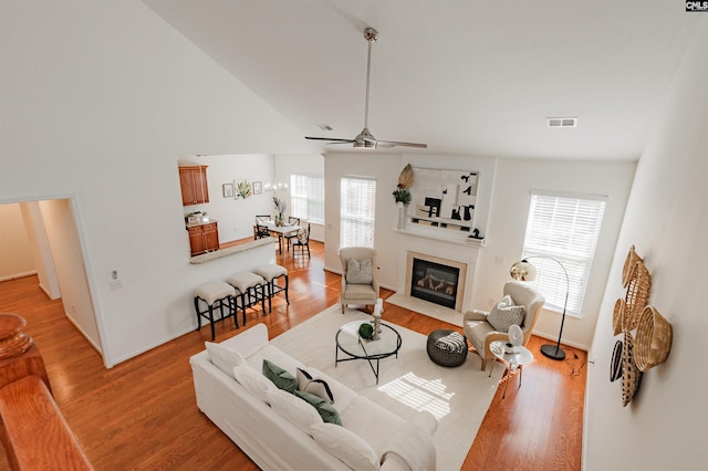 living area with light wood finished floors, visible vents, ceiling fan, a fireplace with flush hearth, and lofted ceiling