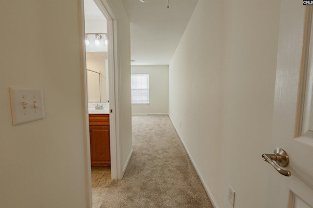 corridor featuring light colored carpet, baseboards, and a sink