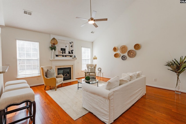 living area with wood finished floors, a ceiling fan, visible vents, baseboards, and a fireplace with flush hearth