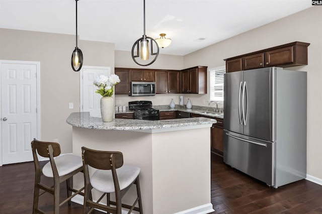 kitchen featuring a sink, a kitchen breakfast bar, dark wood finished floors, stainless steel appliances, and dark brown cabinets