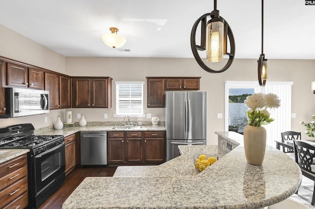 kitchen featuring light stone countertops, dark wood finished floors, decorative light fixtures, appliances with stainless steel finishes, and a sink